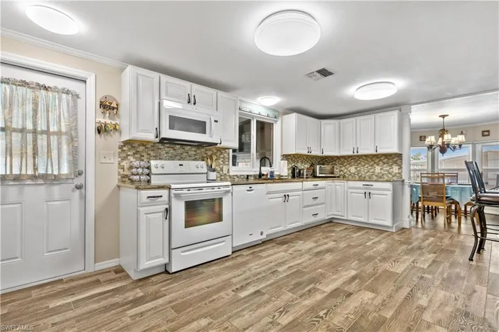 Kitchen with light hardwood / wood-style flooring, crown molding, white cabinets, sink, and white appliances