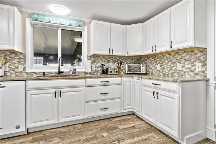 Kitchen featuring white dishwasher, white cabinetry, backsplash, and light wood-type flooring