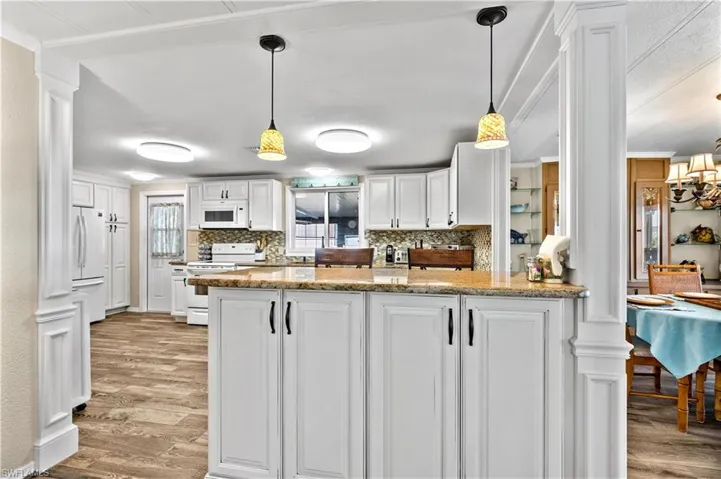 Kitchen with decorative light fixtures, light hardwood / wood-style floors, white appliances, and white cabinetry
