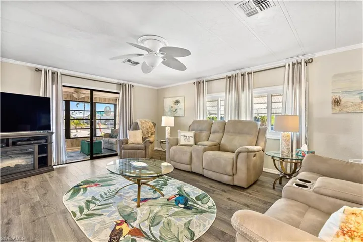 Living room with ceiling fan, ornamental molding, a wealth of natural light, and wood-type flooring
