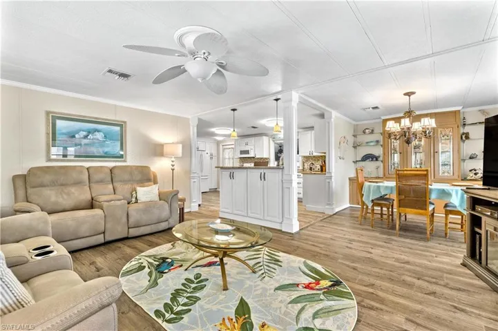 Living room with ornamental molding, light hardwood / wood-style flooring, and ceiling fan with notable chandelier