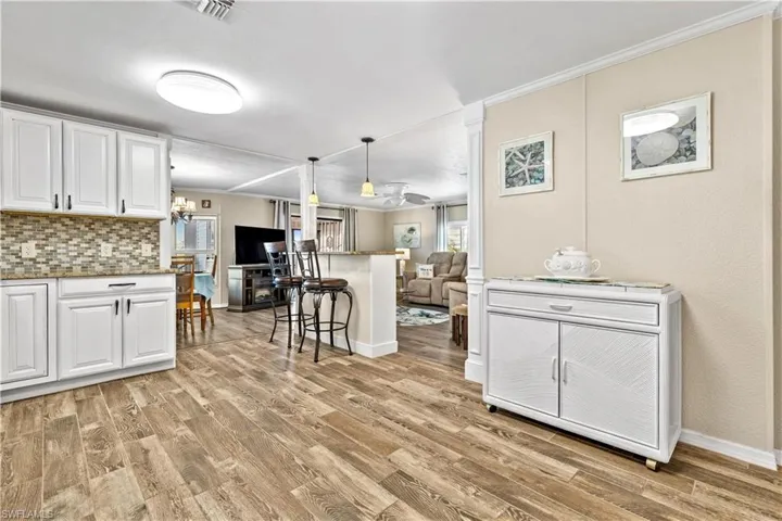Kitchen featuring light hardwood / wood-style floors, tasteful backsplash, decorative light fixtures, a breakfast bar, and white cabinets