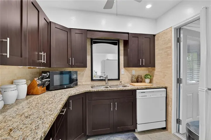 Kitchen with dark wood finish cabinetry, white appliances, light stone counters, ceiling fan, and recessed lighting