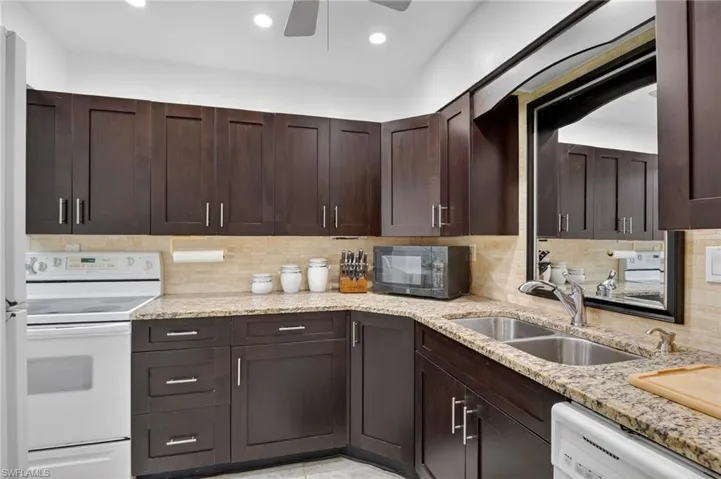 Kitchen featuring dark wood finish cabinets, white appliances, light stone countertops, ceiling fan, and recessed lighting