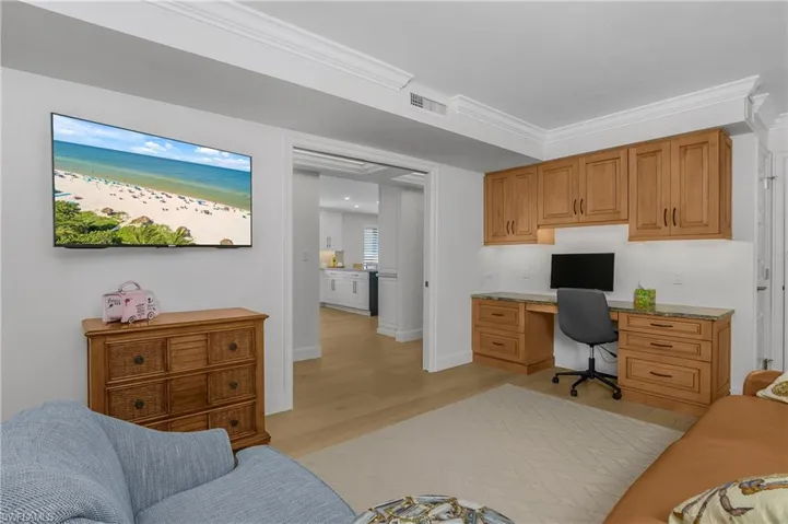 3rd bedroom currently used as an office area, with built in study area, light wood floors, and ornamental molding, leather pull out sofa, new hurricane window and a closet.