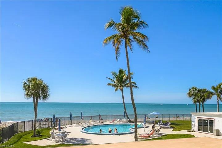 Embassy Club pool featuring a relaxing patio area, gated beach access, a water view, and a fenced backyard