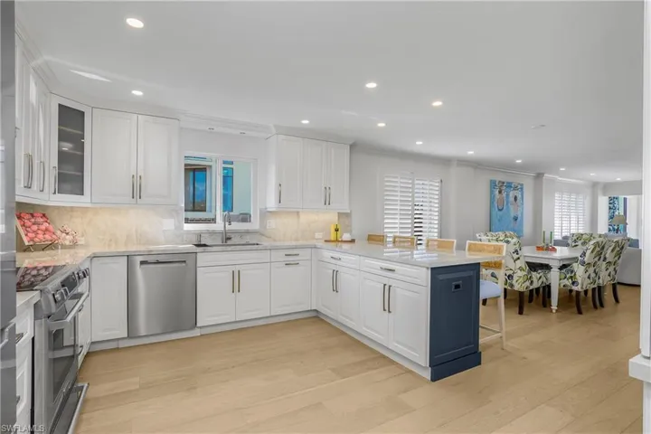 Kitchen featuring a kitchen bar, a peninsula, stainless steel appliances, light wood flooring, and white cabinetry, with storage pantry and coffee bar cabinetry