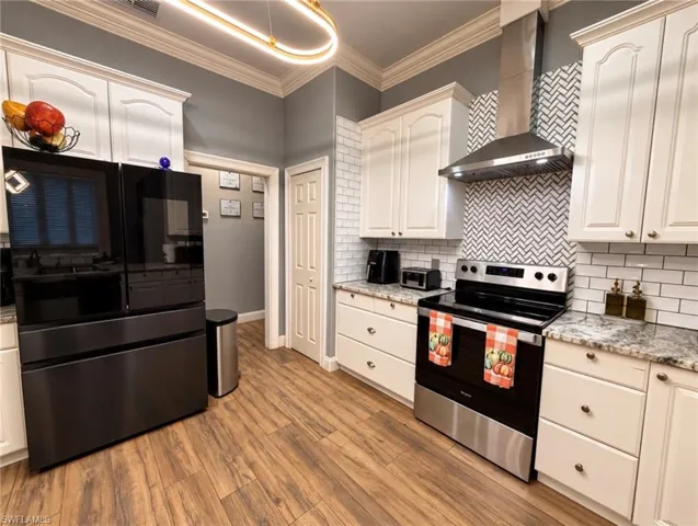 Kitchen featuring off-white cabinetry, stone-finish countertops, stainless steel appliances, herringbone-patterned tile backsplash, and wood-finish flooring