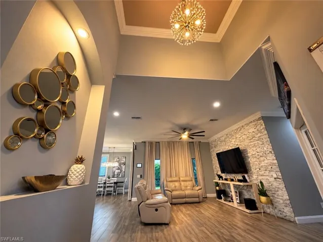 High-ceiling living area featuring a stacked-stone accent wall, wood-finish flooring, a decorative tray ceiling, and a multi-bulb statement chandelier