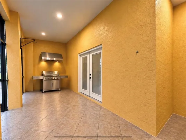 Covered patio featuring ceramic tile flooring, built-in stainless steel grill, stainless steel vent hood, and double-door entry