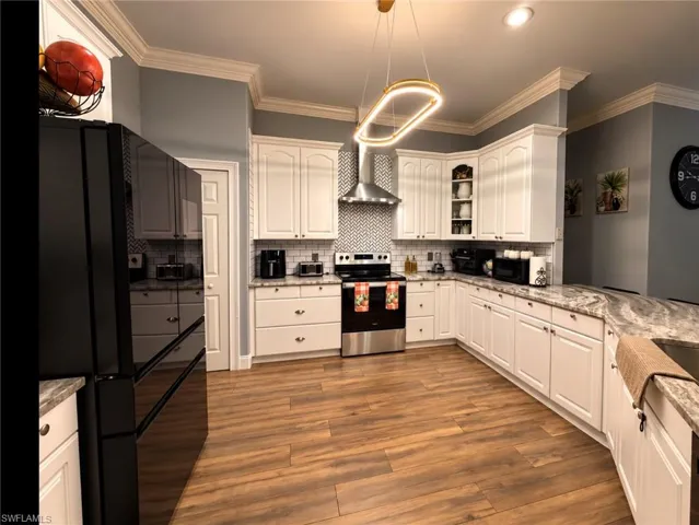 Kitchen featuring white cabinetry, wood-finish flooring, stone-patterned countertops, a stainless steel range with a matching chimney hood, and a geometric-patterned tile backsplash
