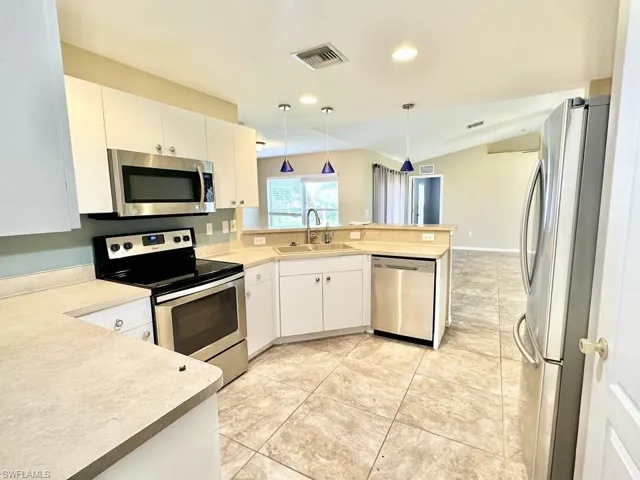 Kitchen with stainless steel appliances, pendant lighting, white cabinetry, light countertops, and vaulted ceiling