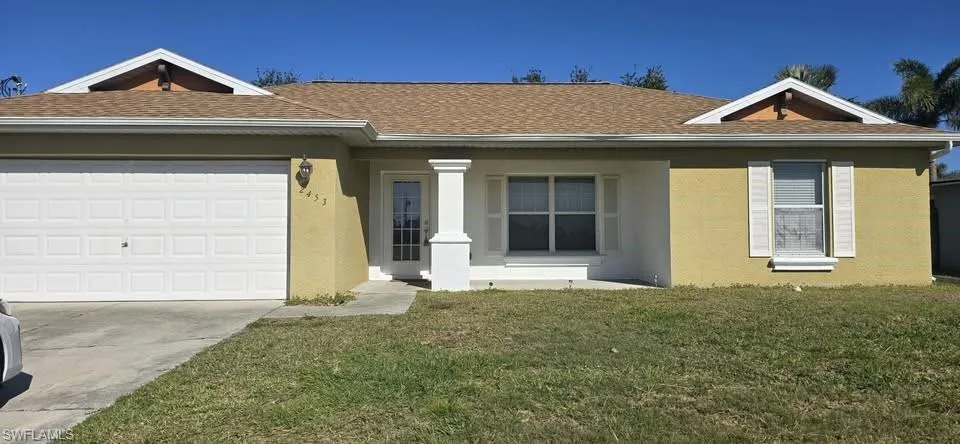 Ranch-style home featuring a front lawn, covered porch, stucco siding, driveway, and a garage