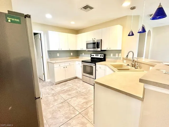 Kitchen featuring stainless steel appliances, a peninsula, decorative light fixtures, arched walkways, and light countertops