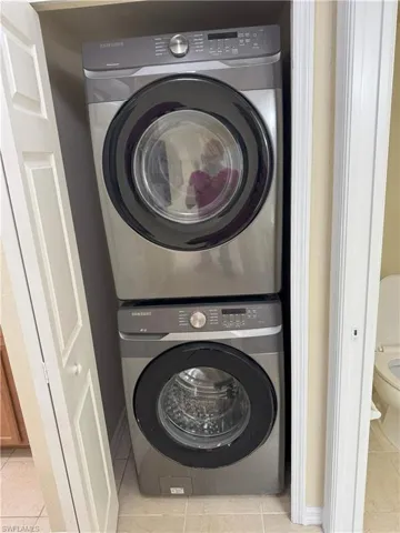 Clothes washing area with stacked washer and dryer and light tile patterned floors