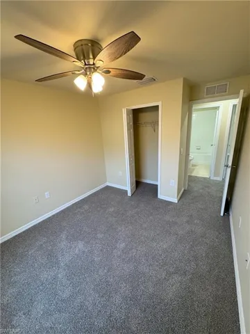 Unfurnished bedroom featuring dark colored carpet, ceiling fan, and a closet