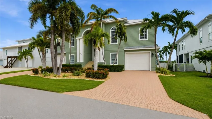 Two-story exterior with siding, arched entry, paver driveway, attached garage, and established landscaping - Virtually Edited Image
