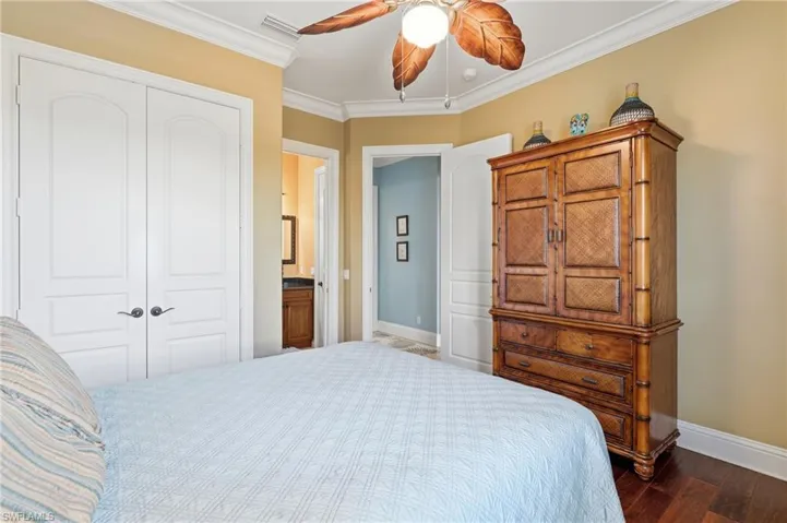 Spacious primary bedroom featuring warm yellow walls, hardwood flooring, a decorative ceiling fan with leaf-shaped blades, and abundant natural light - Virtually Edited Image