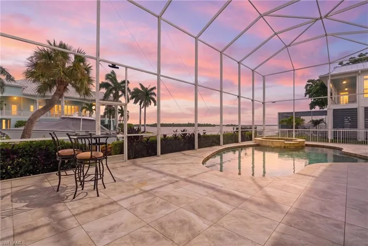Expansive screened lanai with travertine tile flooring and structural glass panels framing panoramic sunset vistas - Virtually Edited Image