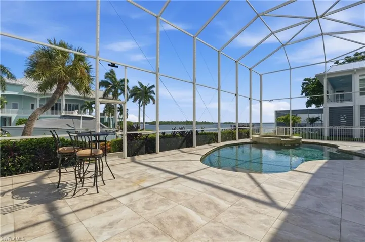 Screened outdoor living area featuring a freeform pool with integrated spa, expansive paver patio, and lush perimeter landscaping - Virtually Edited Image