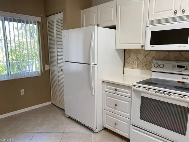 Kitchen featuring light tile patterned floors, white cabinetry, backsplash, freestanding refrigerator, and range