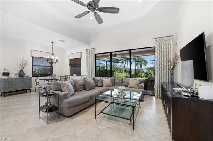 Living room featuring a raised ceiling, crown molding, light tile patterned floors, and ceiling fan with notable chandelier