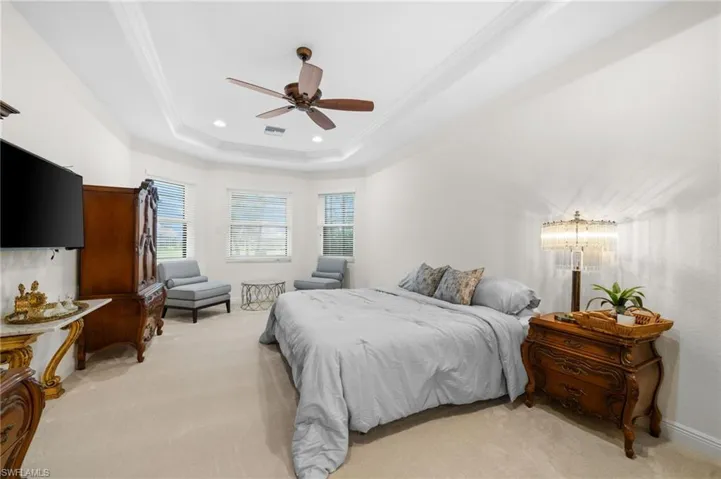 Carpeted bedroom with a raised ceiling, ceiling fan, and ornamental molding