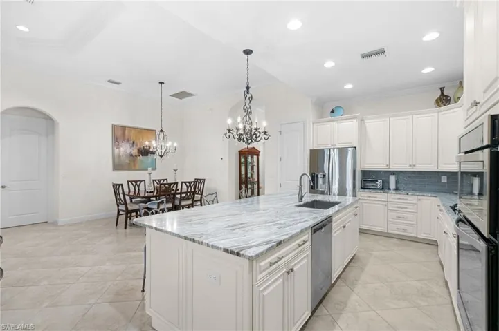 Kitchen featuring backsplash, light stone counters, stainless steel appliances, a center island with sink, and white cabinets