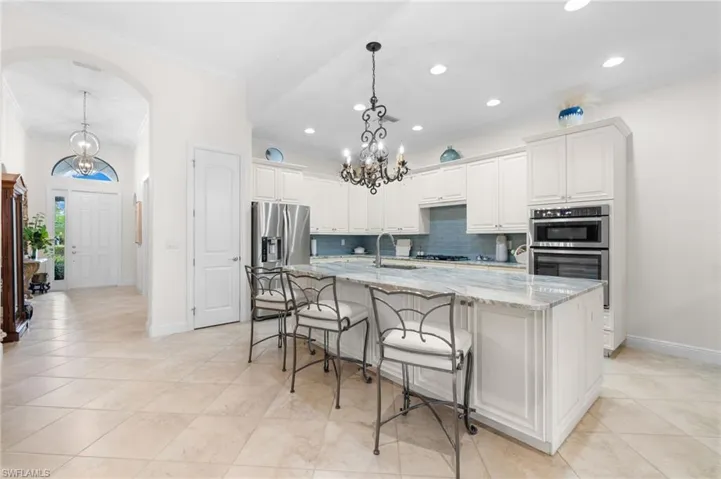 Kitchen with tasteful backsplash, light stone counters, a large island with sink, pendant lighting, and white cabinets