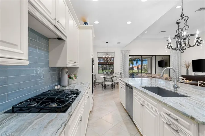 Kitchen with backsplash, white cabinets, black gas stovetop, sink, and light stone counters