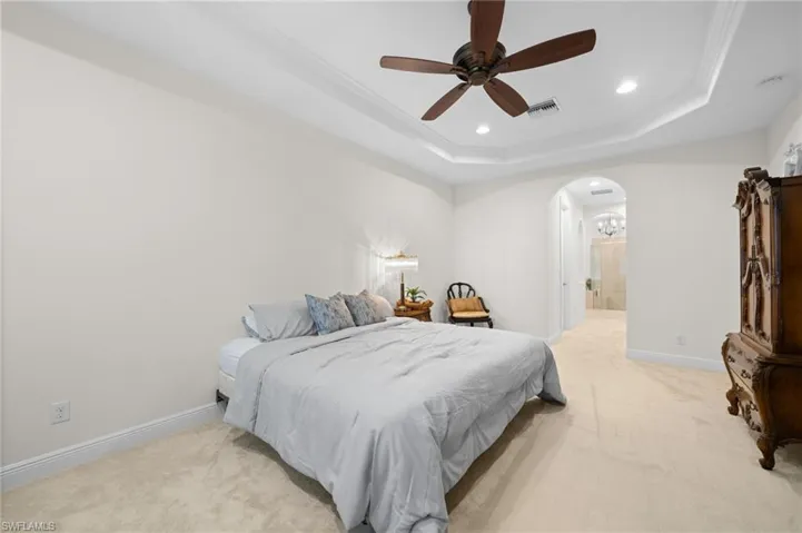 Bedroom with ceiling fan, a raised ceiling, light carpet, and connected bathroom