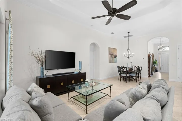 Tiled living room with ceiling fan with notable chandelier and ornamental molding