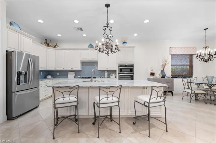 Kitchen with light stone countertops, an inviting chandelier, pendant lighting, a center island with sink, and appliances with stainless steel finishes