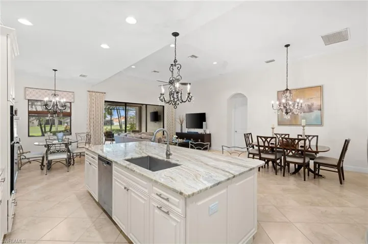 Kitchen featuring a kitchen island with sink, sink, stainless steel dishwasher, light stone countertops, and white cabinetry