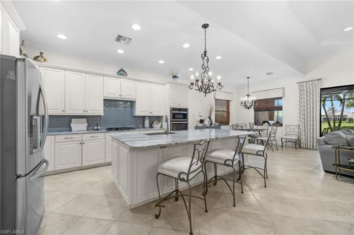 Kitchen featuring pendant lighting, white cabinets, light stone countertops, an island with sink, and appliances with stainless steel finishes