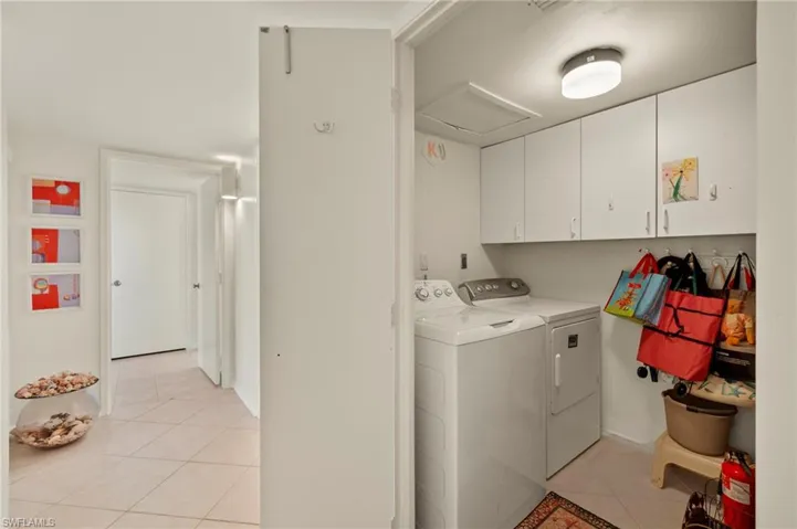 Laundry area featuring light tile patterned floors, cabinet space, and washing machine and clothes dryer