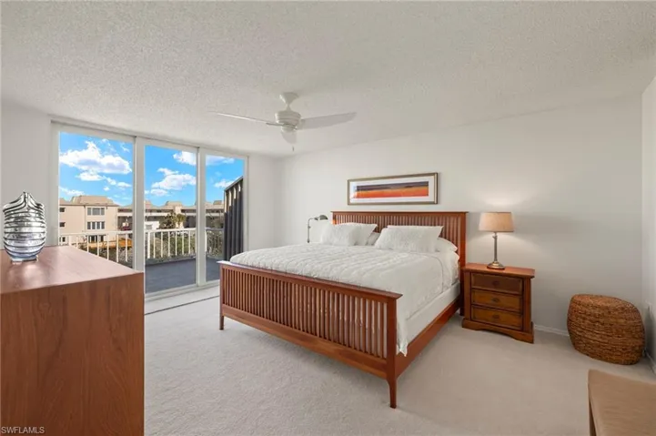 Bedroom with carpet floors, a textured ceiling, access to exterior, a wall of windows, and ceiling fan