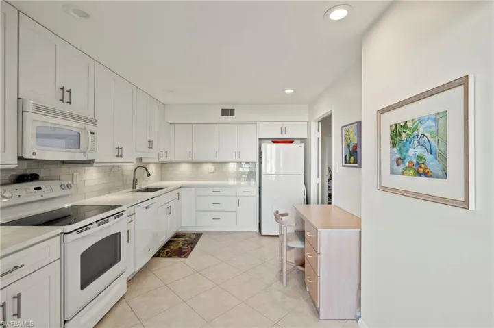 Kitchen with white appliances, white cabinets, backsplash, light tile patterned floors, and recessed lighting