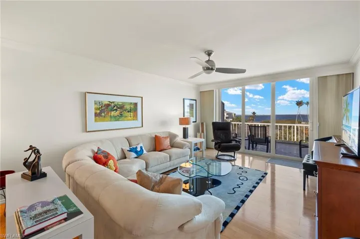 Living area with ornamental molding, light wood-style floors, ceiling fan, and expansive windows