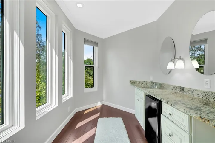 Bar area featuring light stone countertops, dark wood-style floors, healthy amount of natural light, and white cabinetry
