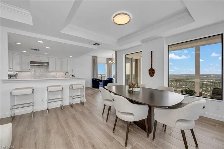 Dining room featuring a notable chandelier, light hardwood / wood-style floors, ornamental molding, and a tray ceiling