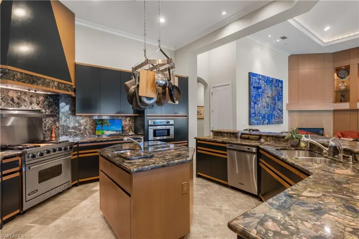 Kitchen with a kitchen island with sink, stainless steel appliances, dark stone countertops, sink, and premium range hood
