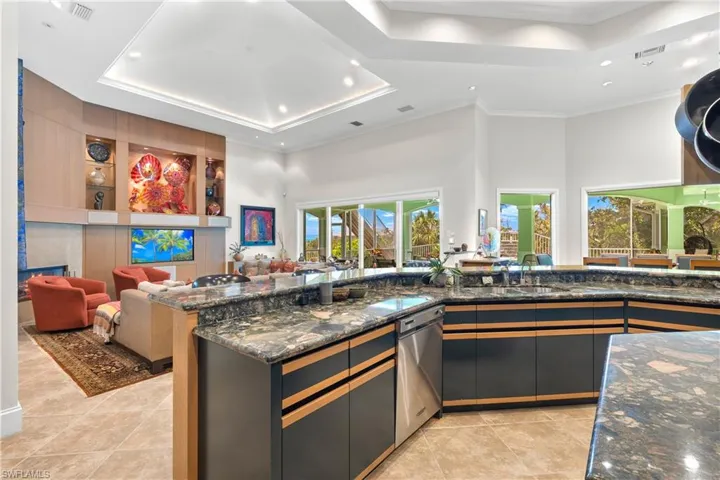 Kitchen featuring a towering ceiling, light tile patterned flooring, a raised ceiling, stainless steel dishwasher, and dark stone countertops