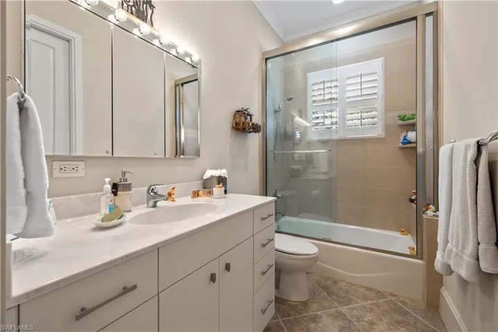 Full bathroom featuring tile patterned floors, toilet, ornamental molding, vanity, and shower / bath combination with glass door
