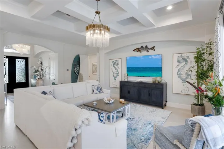 Living area featuring a chandelier, coffered ceiling, arched walkways, and crown molding