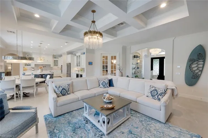 Living room featuring hanging lights, ornamental molding, coffered ceiling, and arched walkways