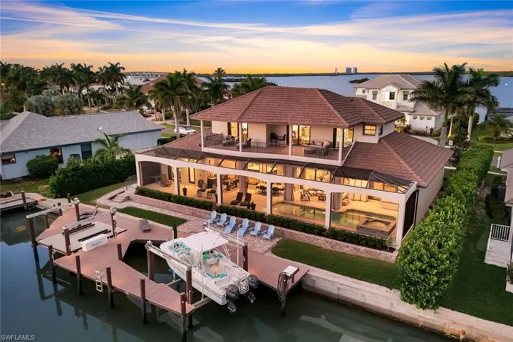 Back of house at dusk featuring a patio area, boat lift, an outdoor pool, a water view, and stucco siding