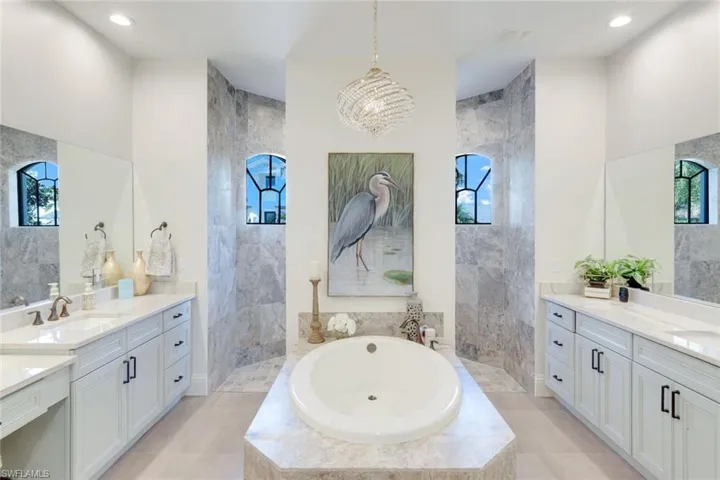 Bathroom featuring a bath, walk in shower, two vanities, and suspended lighting