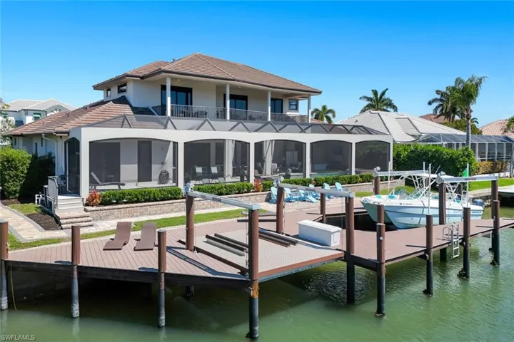 Dock featuring a water view, a sunroom, boat lift, and a balcony