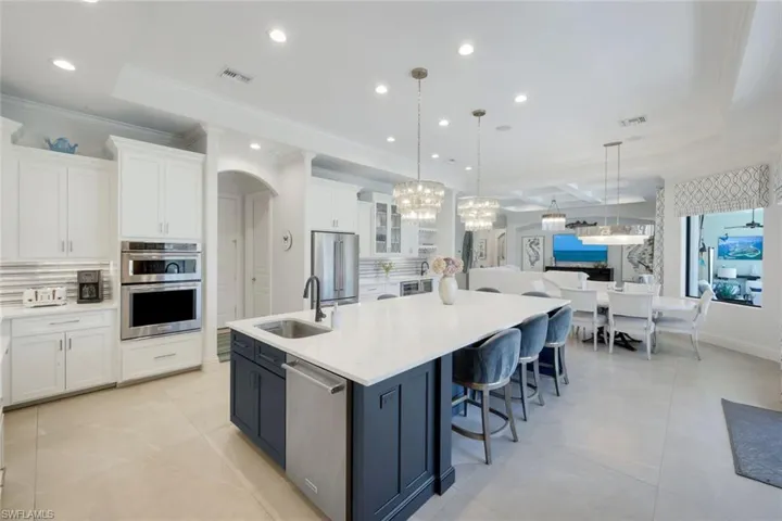 Kitchen featuring two tone cabinetry, backsplash, a large island, light stone counters, and stainless steel appliances